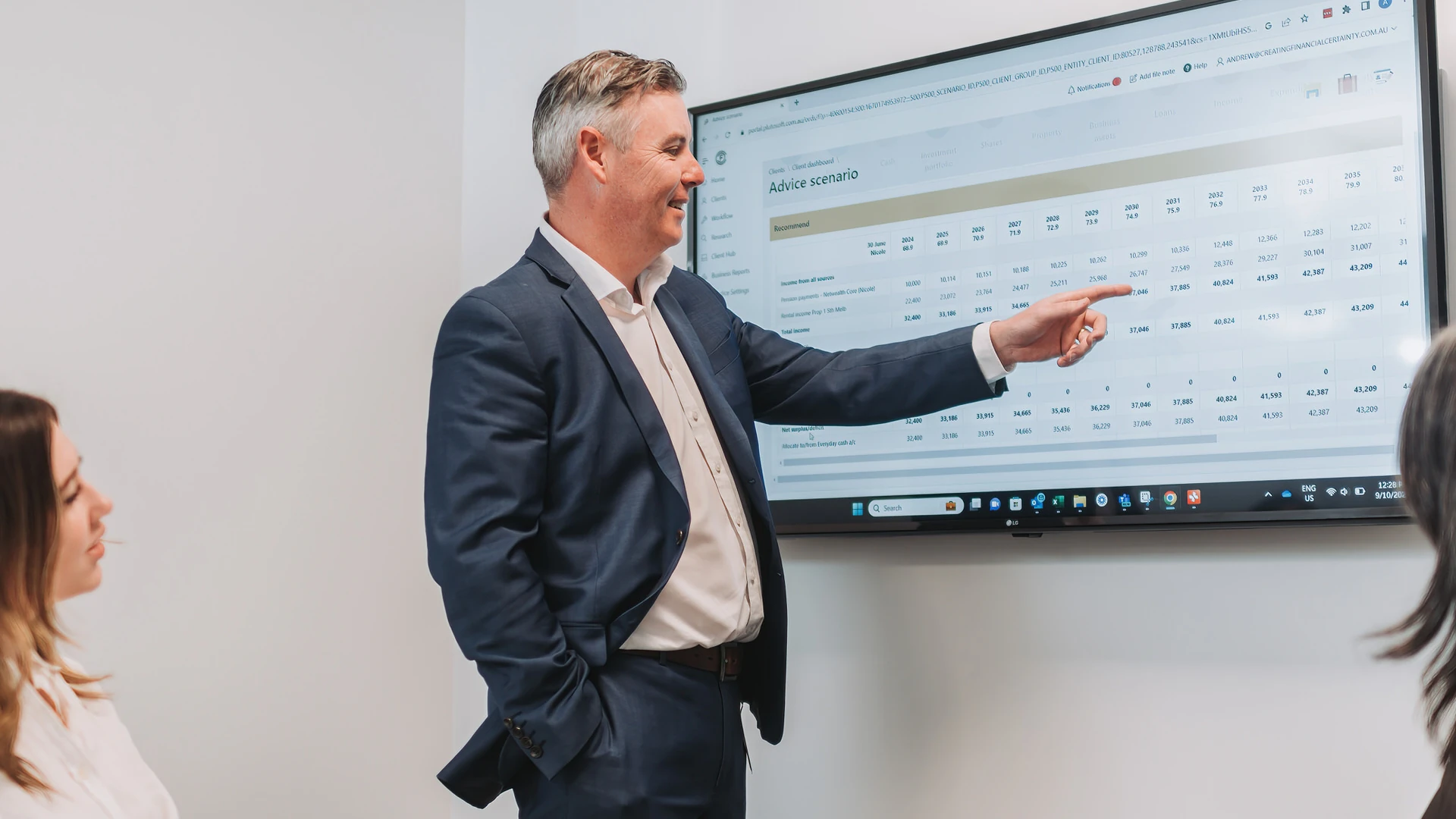 A group of three staff members with one person pointing at a monitor on the wall.